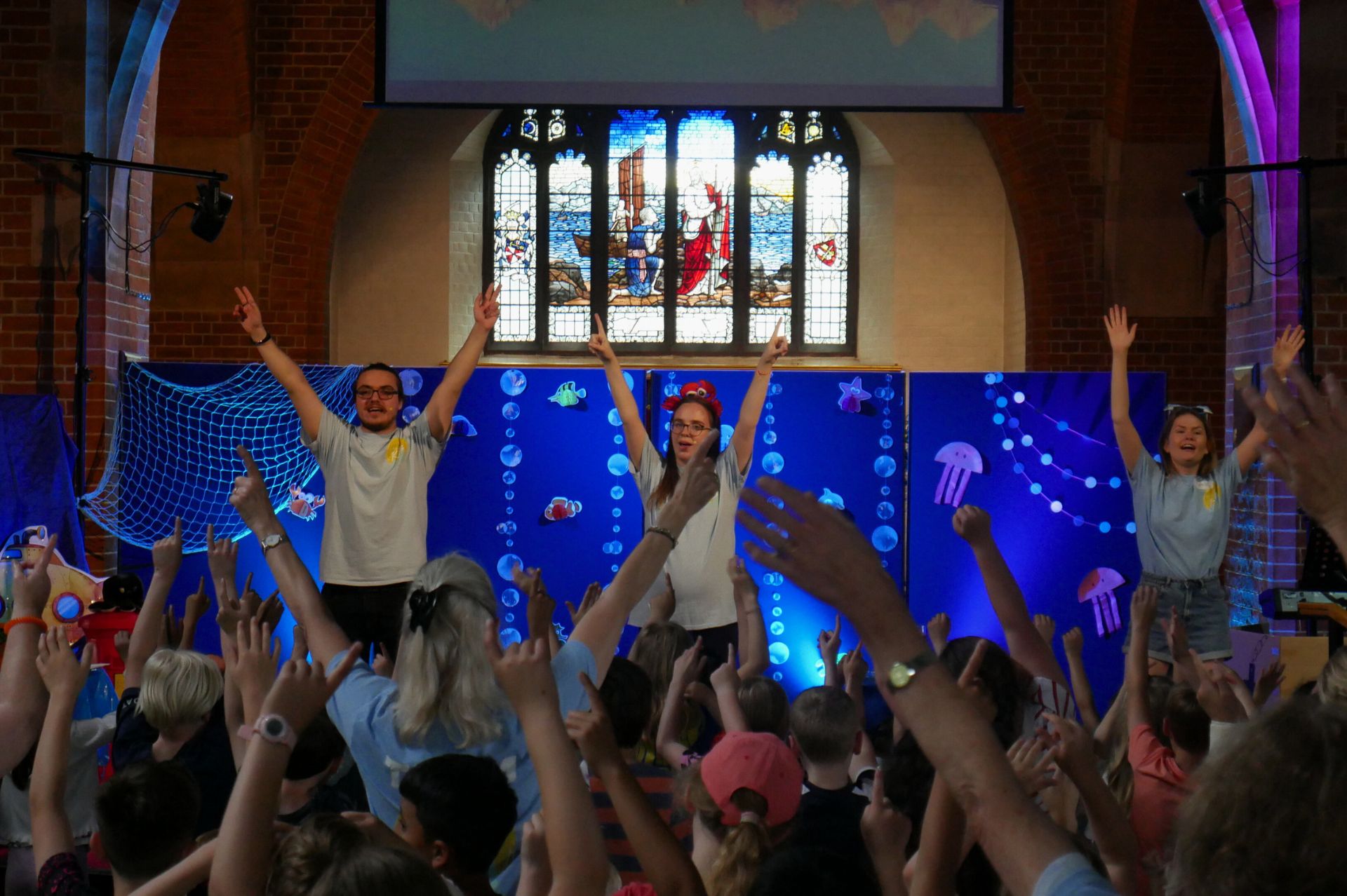 A group of adults leading actions on a stage in front of a crowd of children joining in