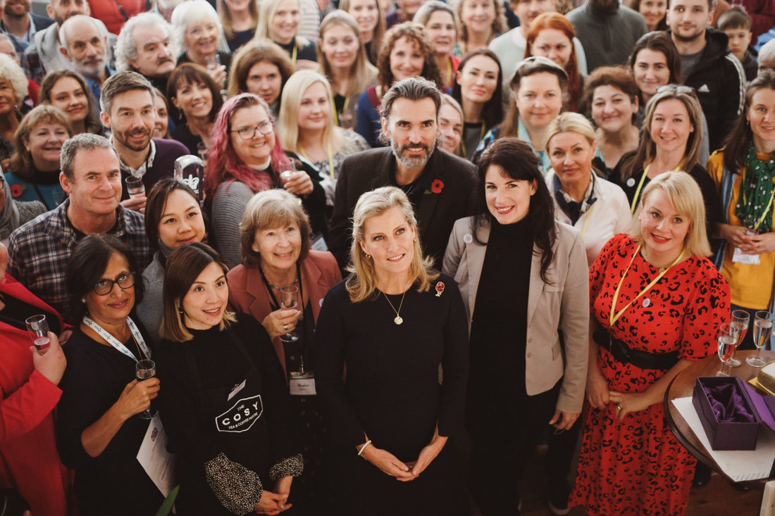 A large group of people gathererd around Sophie Wessex, smiling and posing for a photo