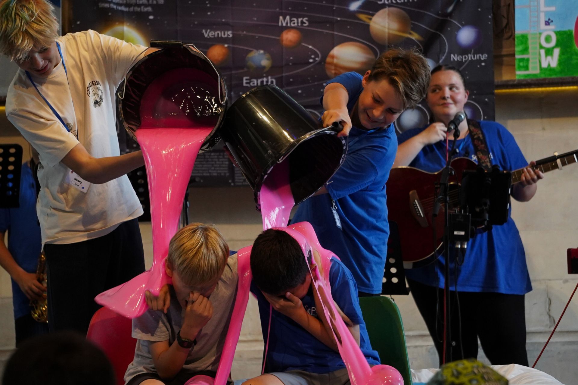 Two young people having buckets of pink gunge poored over them