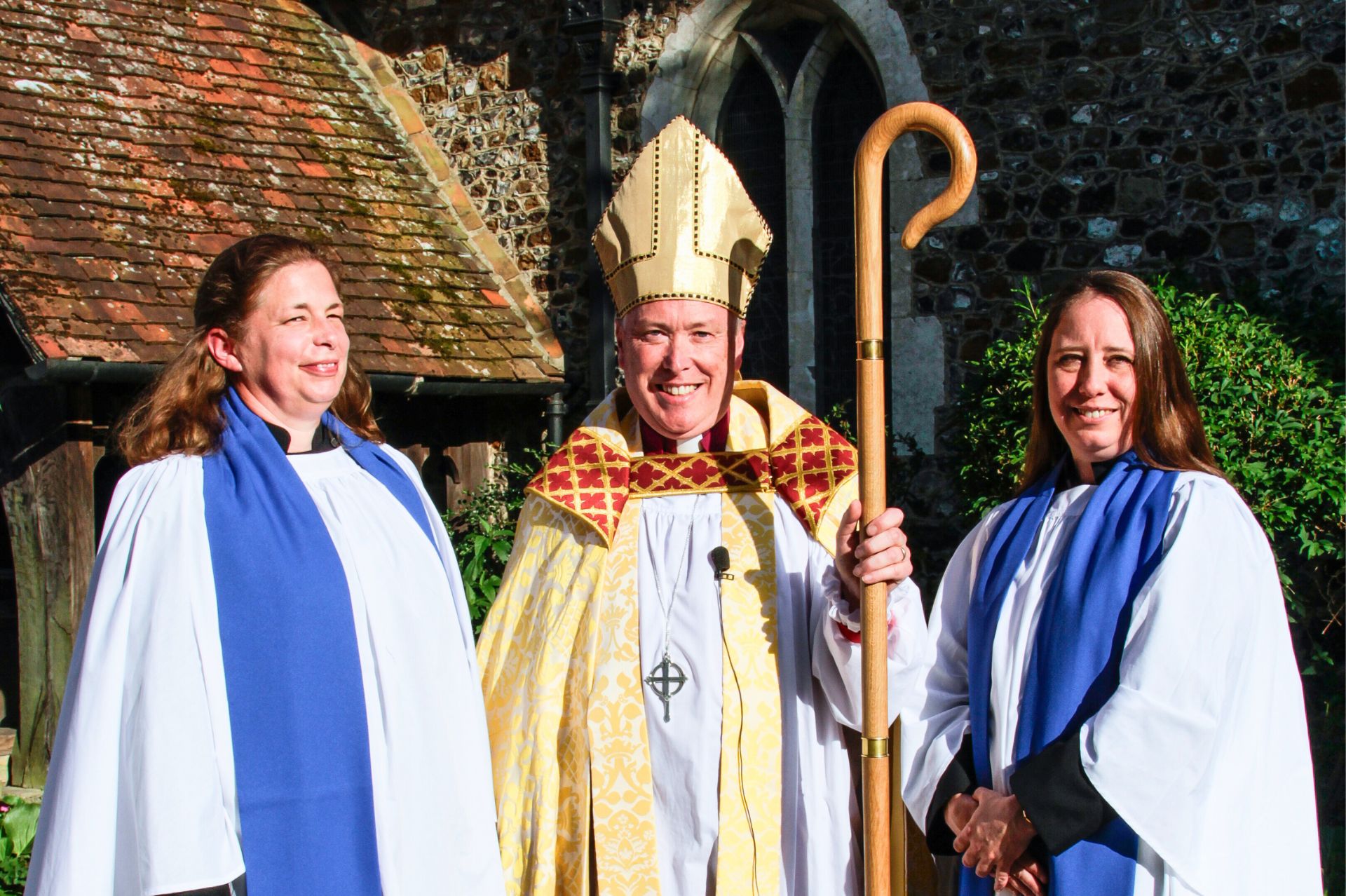 Sam Fisk and Amber Wood sttod with Bishop Paul Davies outside a church building, all in clerical robes