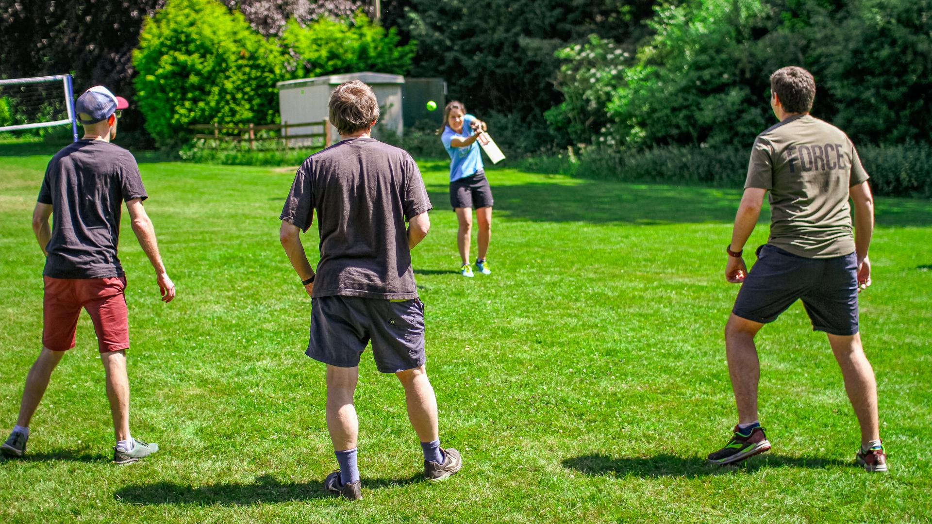Groups of people playing French cricket in a green field surrounded by green trees