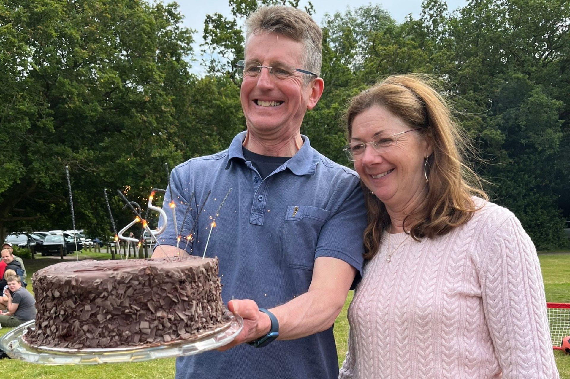 George and Jane Newton holding a homemade cake with a 25 sparkler on