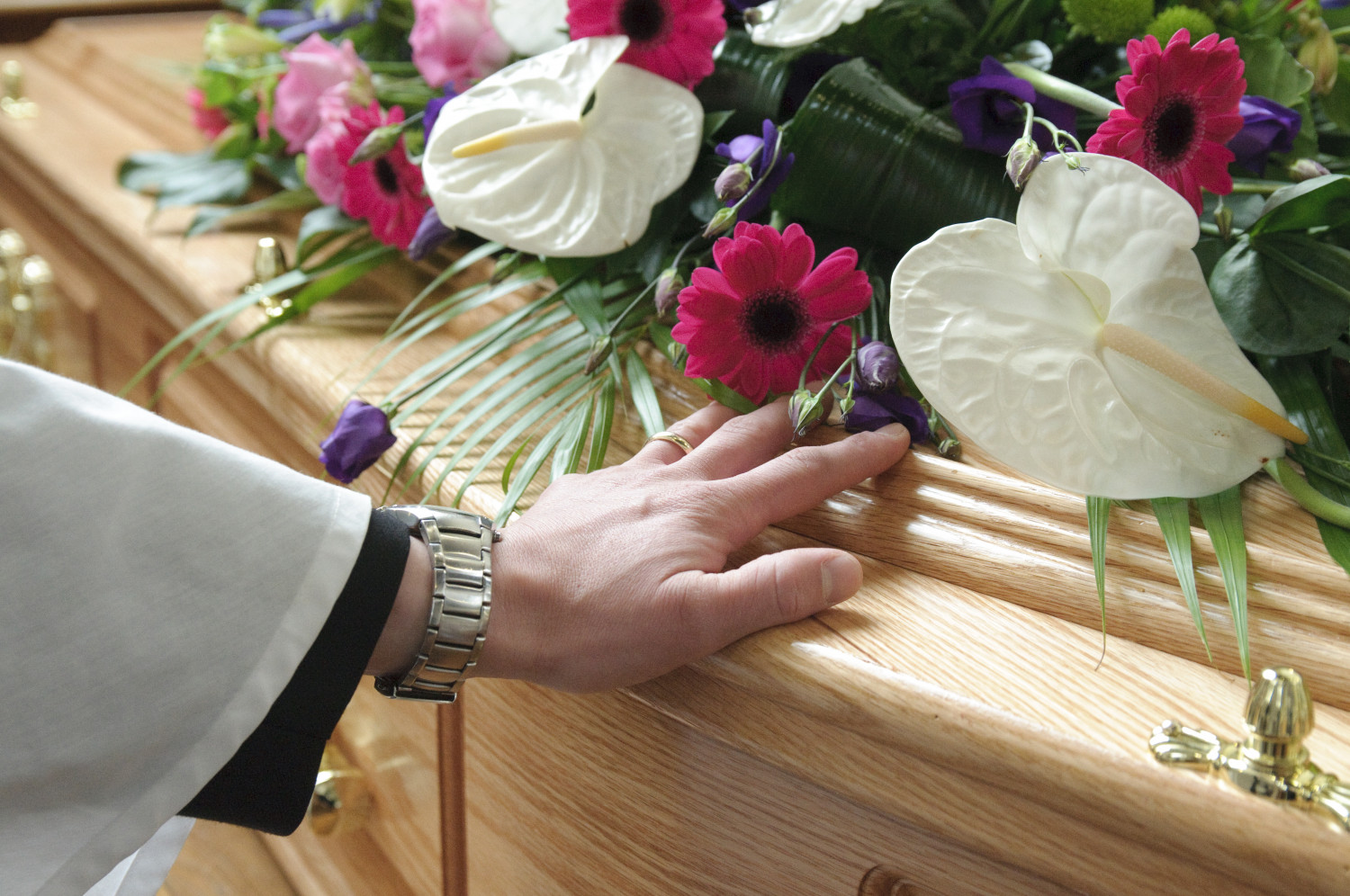 A hand resting on a coffin laid with pink, white and purple flowers