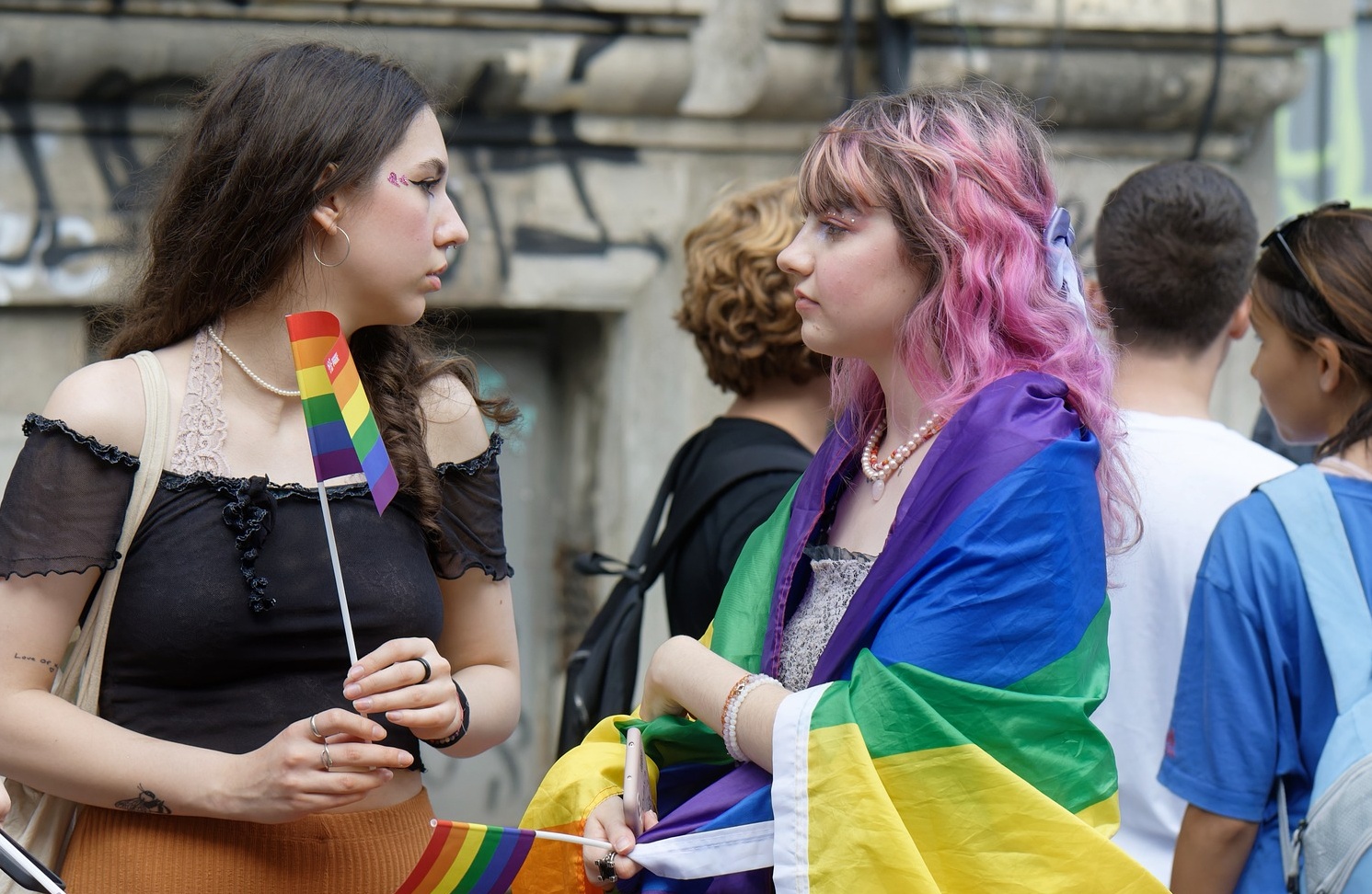 Two teenage girls wearing and holding the rainbow flag at a pride march